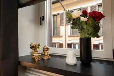 a window sill with a vase with roses and gold statues at Acque Romane Fontana di Trevi M in Rome