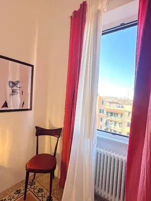 a room with a chair and a window with red curtains at Clarus apartment in Rome in Rome