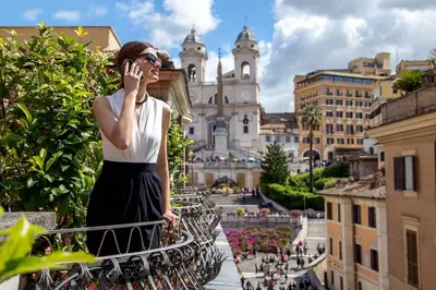 a woman talking on a cell phone on a balcony at The Inn at the Spanish Steps Exclusive Collection - The Nest Penthouse in Rome