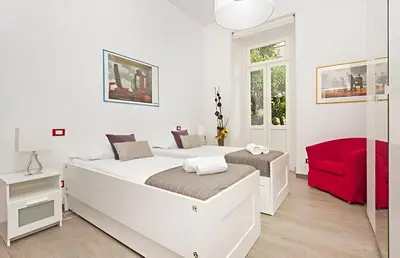 a white bedroom with two beds and a red chair at Ungaretti Vatican Apartment in Rome
