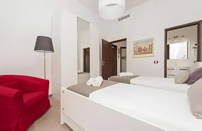 a white room with two beds and a red chair at Ungaretti Vatican Apartment in Rome