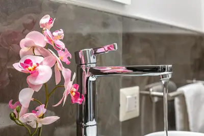 a chrome bathroom sink with pink flowers in a vase at iFlat Brand New & Modern Central Station apt in Rome