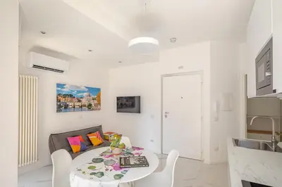 a white living room with a table and a kitchen at Sunrise House - San Paolo in Rome