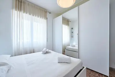 a white bedroom with a bed and a mirror at Modern Comfort Steps from Tiburtina Station in Rome