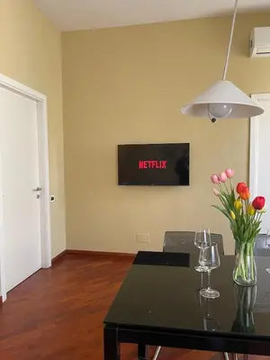 a room with a table with flowers and a tv on the wall at San Giovanni Apartment Rome in Rome