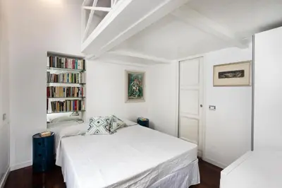 a white bedroom with a bed and a book shelf at Your nest with wooden ceilings in Monti in Rome