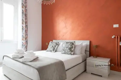 a bedroom with a white bed with an orange wall at Lucky's House - 400mt to Metro A, 3 bedrooms, 6-8 pax, A-C, Roma in Rome