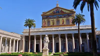 a building with a statue in front of it with palm trees at Sette Chiese Apartment in Rome