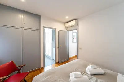 a white bedroom with a bed and a red chair at Piazza Navona the most central apartment in Rome
