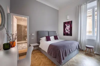 a white bedroom with a bed and a chair at DA ME Suites in Rome