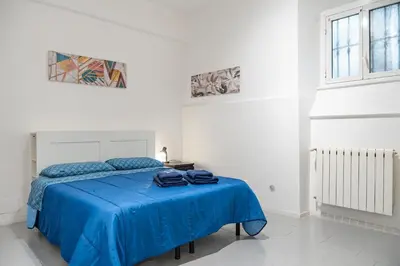 a white room with a bed with blue sheets at Lion Renting Vatican Apartment in Rome