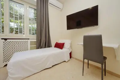 a bedroom with a bed with a chair and a flat screen tv at Vatican Rooms Mura Aurelie in Rome