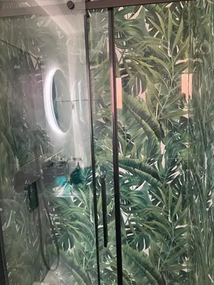 a bathroom with a glass shower with green plants on the wall at Esquilino rooms in Rome