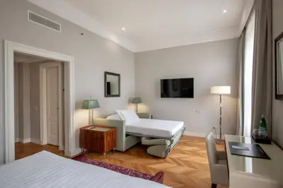 a bedroom with a bed and a table and a tv at Rose Garden Palace Roma by OMNIA hotels in Rome