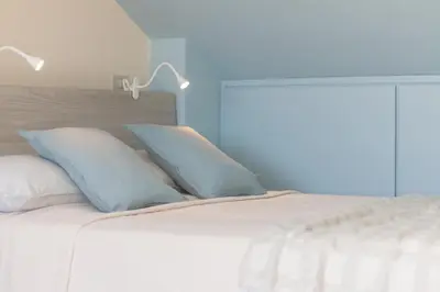 a white bed with two blue pillows and two lamps at Luxury Maison Dei Colli in Rome