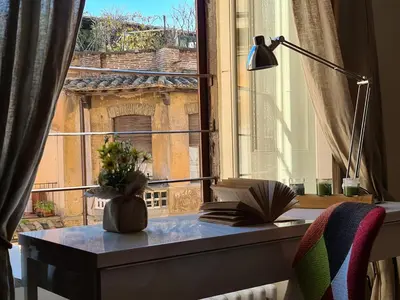 a desk with a book and a vase of flowers next to a window at Boutique Domus Charme Trastevere Vascellari in Rome
