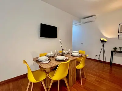 a dining room table with yellow chairs and a television at Gandino House at Vatican in Rome