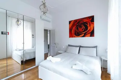 a white bedroom with a large bed with a red rose on the wall at Hermès Apartment Rome in Rome