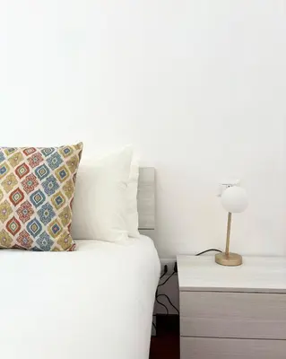 a white bed with a pillow and a lamp on a night stand at Casa Alice Near Vatican City - Modern, High Floor with View in Rome