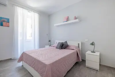 a white bedroom with a pink bed and a window at Domus Ponte Lungo in Rome