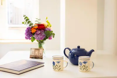 a table with a book and two cups and a vase of flowers at Amazing Via del Corso 277 Suites in Rome