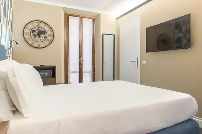 a white bed in a room with a clock on the wall at Dei Greci Guesthouse in Rome