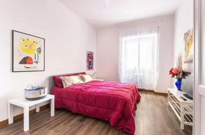 a white bedroom with a red bed and a window at House in the shopping street at Trastevere station in Rome