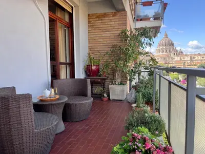 a balcony with wicker chairs and a table with a view of the dome at Roma San Pietro - Elegante appartamento con vista in Rome