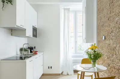 a kitchen with white cabinets and a table with a vase of flowers at iFlat Vatican Modern & Comfortable Peaceful Gem in Rome