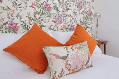 two orange pillows on a bed with a floral wallpaper at Rifugio segreto nel cuore di Roma in Rome