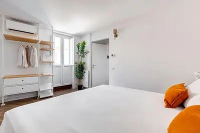 a white bedroom with a large white bed with orange pillows at Domus Gabriella - Roman Forum Apartment in Rome