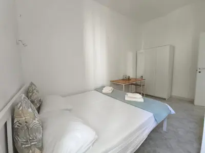 a white bed in a white room with a table at the italians house in Roma San Lorenzo in Rome