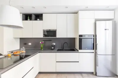 a kitchen with white cabinets and a stainless steel refrigerator at iFlat Sleek & Sunlit Apartment near the Vatican in Rome