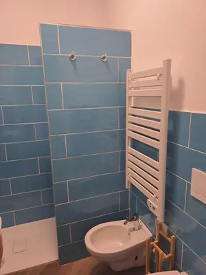 a blue tiled bathroom with a toilet and a sink at At Home Gaeta Guest House in Rome