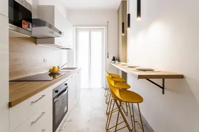 a kitchen with white cabinets and yellow stools at Vacanze romane - Domus chic Trastevere - Marconi by Hôtea in Rome