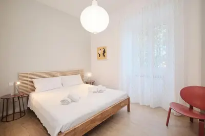 a white bedroom with a large bed and a red chair at Pop Domus Guest House o Affittacamere in Rome