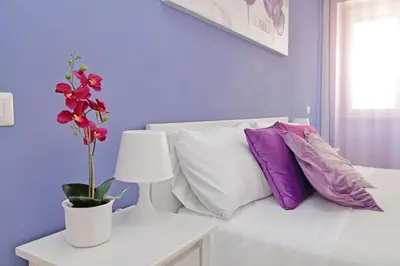 a white bed with purple pillows and a vase with a flower at Victoria Apartment in Rome