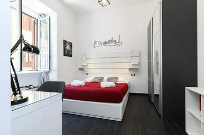 a white bedroom with a red bed and a desk at Casetta di quartiere Roma in Rome