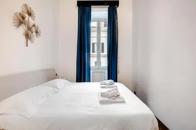 a bedroom with a bed with white sheets and blue curtains at Eleganza e charme a due passi da Piazza di Spagna in Rome