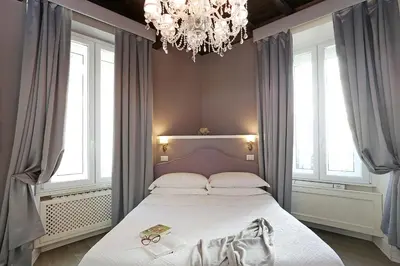 a bedroom with a bed with a chandelier and windows at Piazzetta de' Monti Suites in Rome