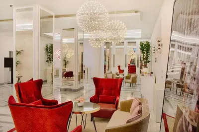a lobby with red chairs and a table and a chandelier at NH Collection Palazzo Cinquecento in Rome