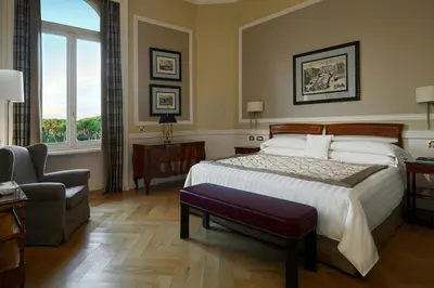 a bedroom with a bed and a chair and a window at Rome Marriott Grand Hotel Flora in Rome