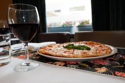 a pizza sitting on a table next to a glass of wine at Giuturna Boutique Hotel in Rome