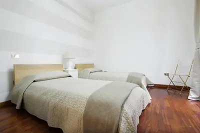 two beds in a white room with wooden floors at Holidays Banchi Nuovi in Rome