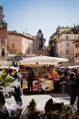 a group of people standing around a market with an umbrella at La Cupola del Vaticano in Rome