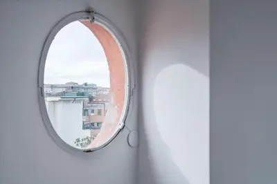 a round mirror on a white wall with a window at Paradiso Penthouse - FromHometoRome in Rome
