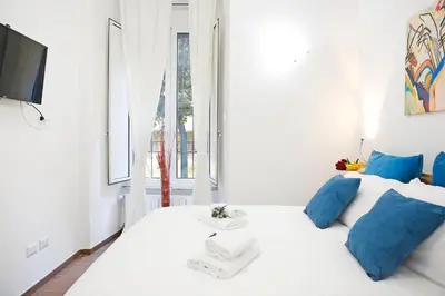 a bedroom with a white bed with blue pillows and a tv at Castel Sant Angelo's Harmonious Apartment in Rome