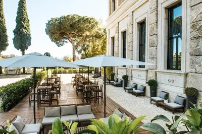 an outdoor patio with tables and chairs and umbrellas at TH Roma - Carpegna Palace in Rome