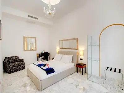 a white bedroom with a bed and a chair at Queen Palace Suites in Rome