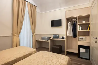 a room with two beds and a desk and a television at Hotel Flavia in Rome